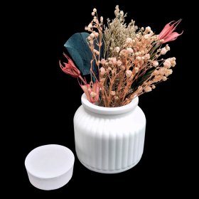 Weißes Gefäß mit Deckel aus aus Raysin mit Trockenblumen vor schwarzem Hintergrund